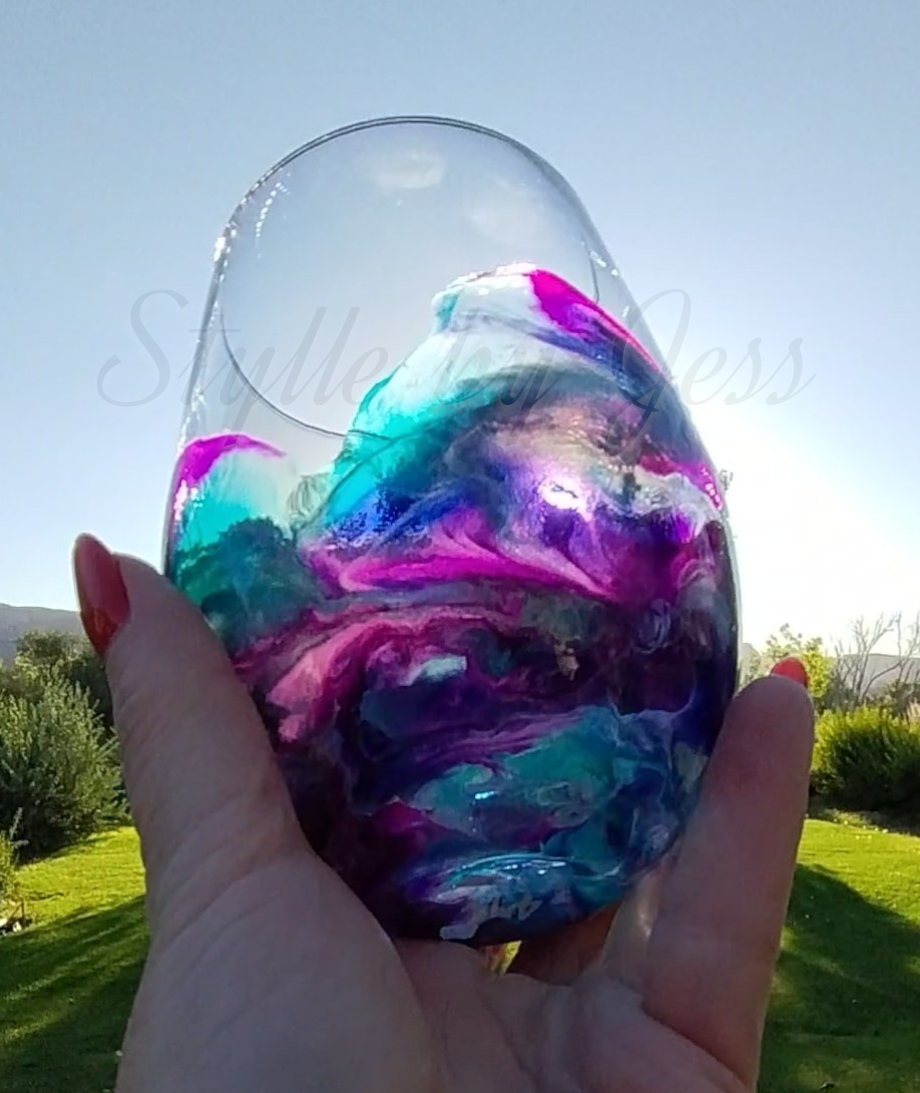 Colorful marbled wine glass held by a hand with a blurred outdoor background