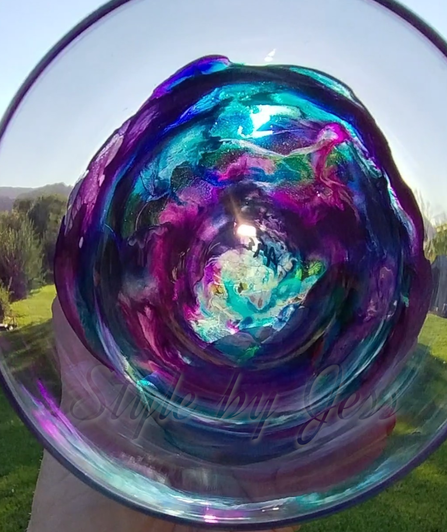 Colorful design showing the abstract art look from inside of the stemless wine glass with swirling patterns held by a person outdoors. A Style by Jess