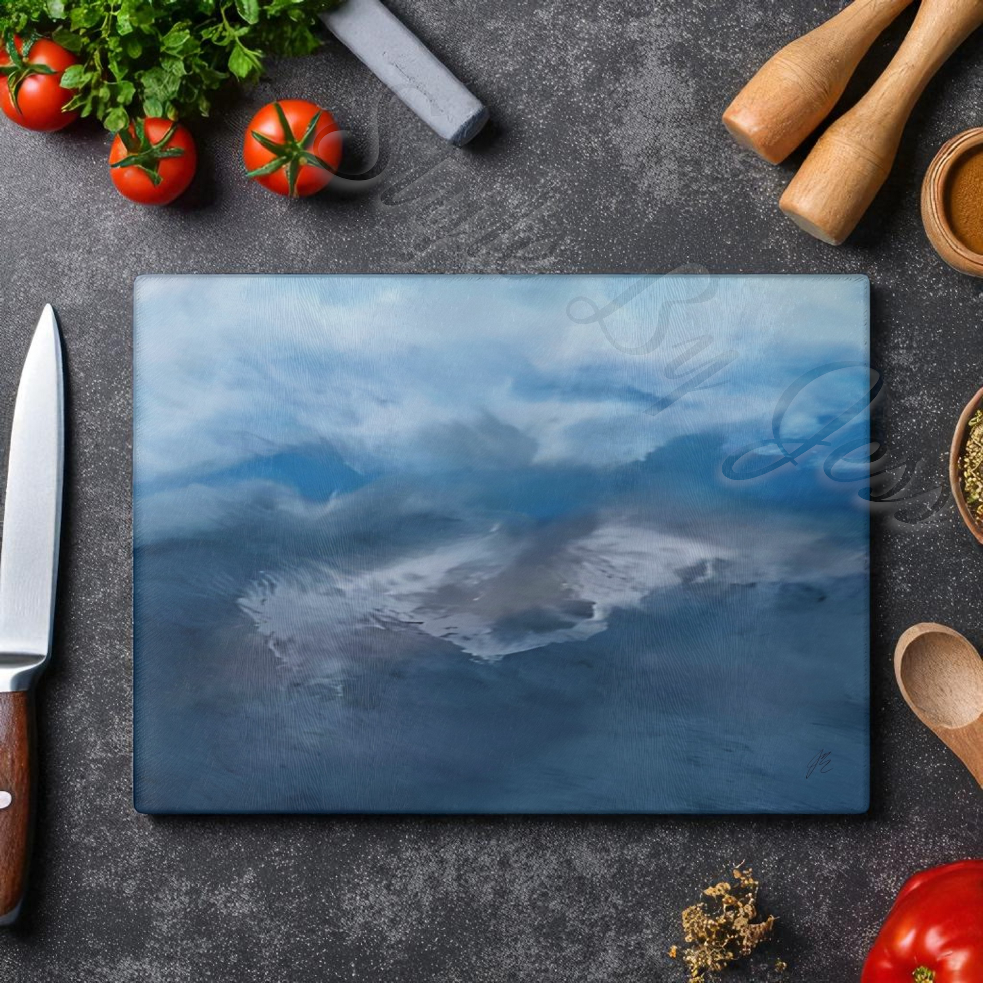 Blue cutting board with a scenic design on a dark surface with kitchen items.