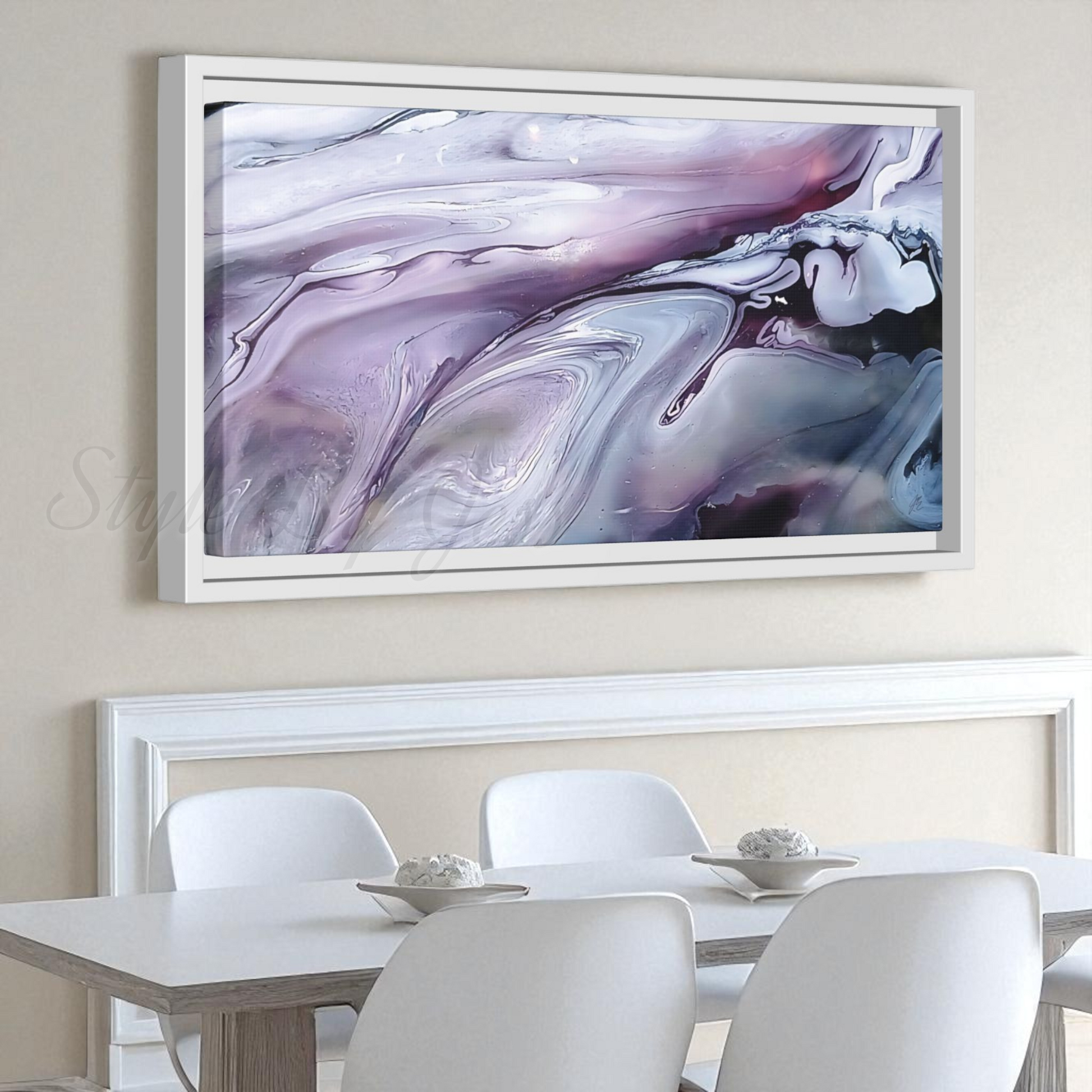 Abstract painting in a white frame on a wall above a dining table with chairs. Style By Jess