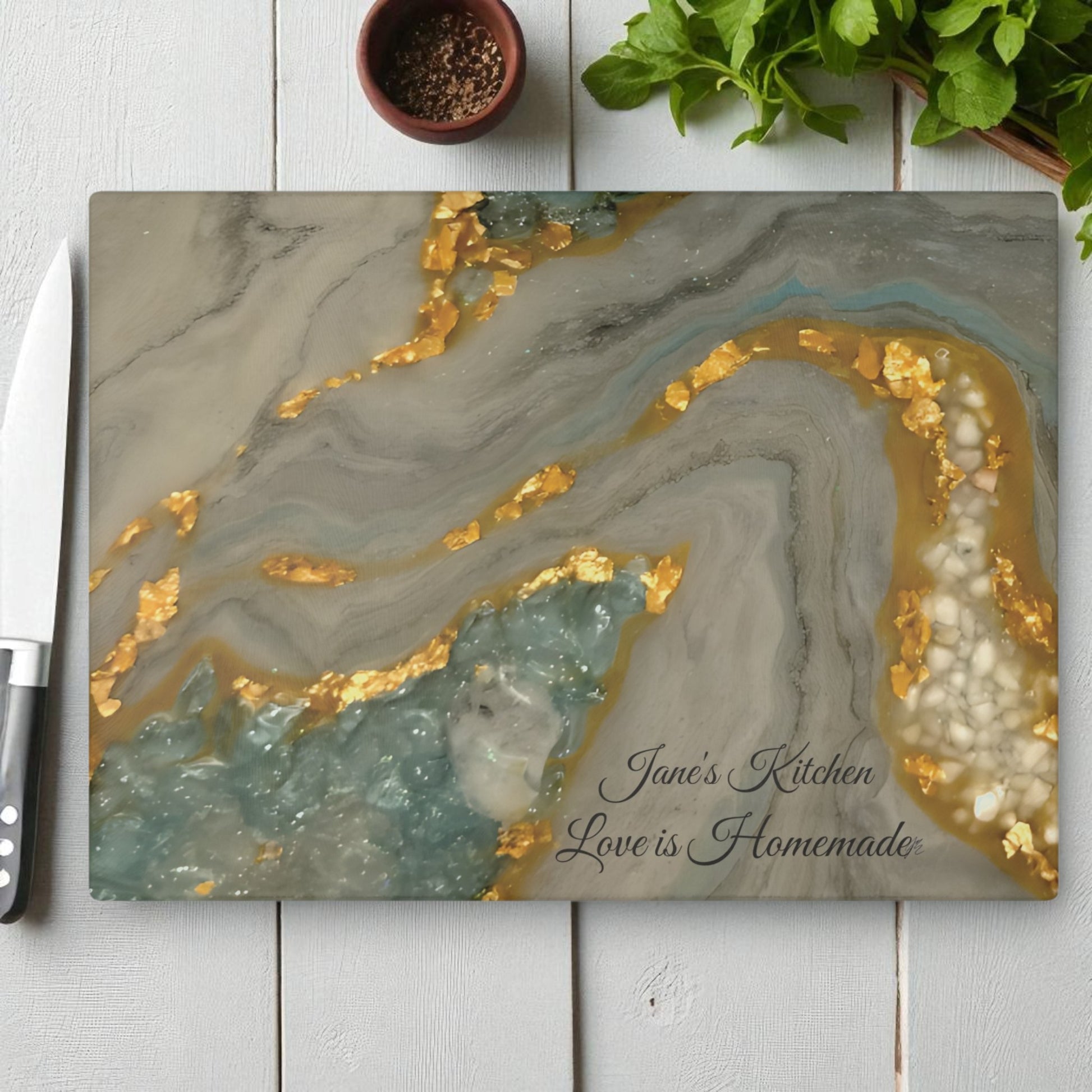 Marble-patterned cutting board with gold and gray design, featuring 'Jane's Kitchen Love is Homemade' text, on a white wooden surface.