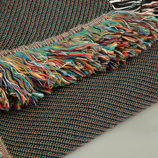 Colorful woven fabric with a fringe on a gray background